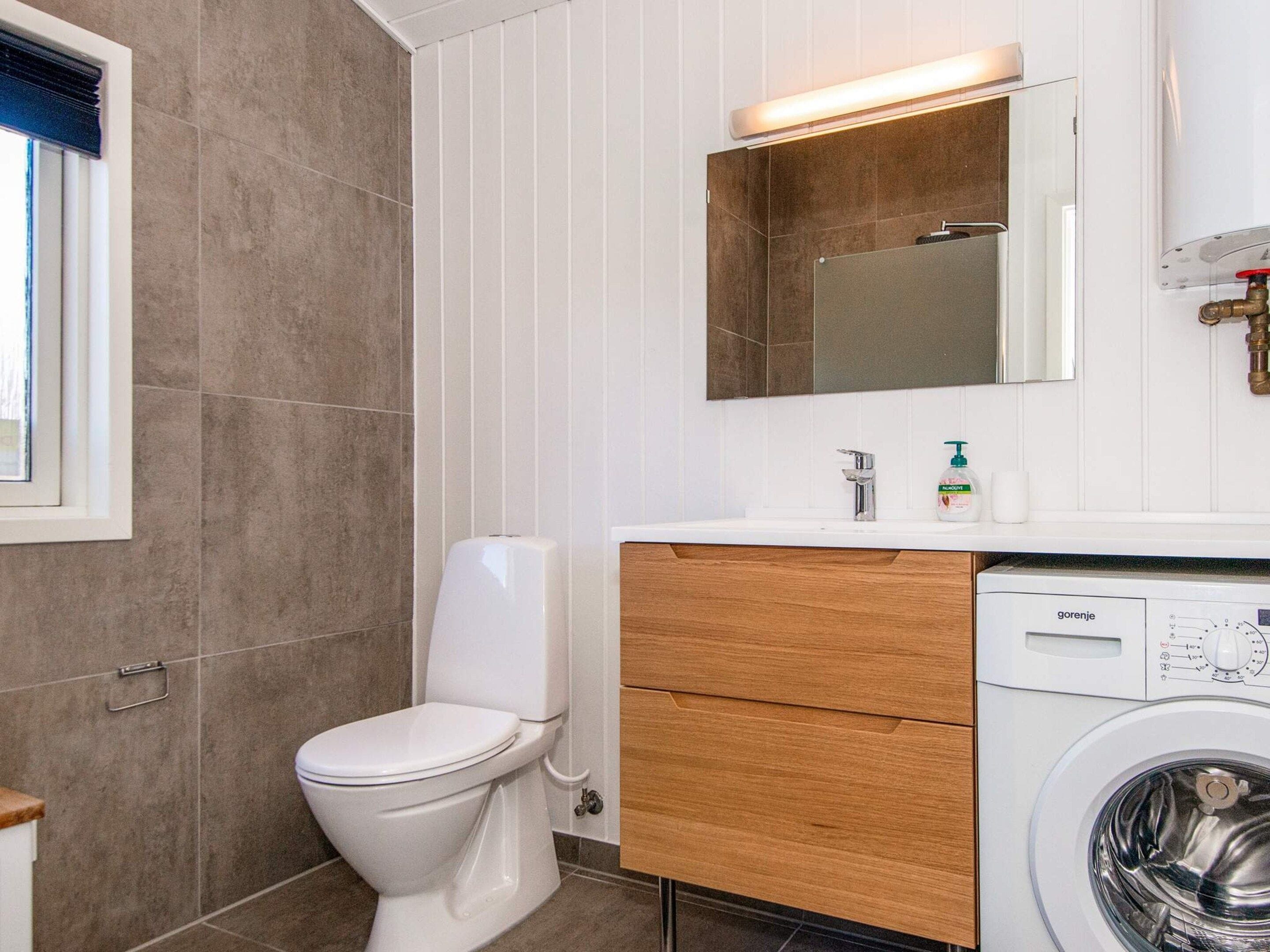 A bathroom with a toilet, a sink, a mirror, and a washing machine.