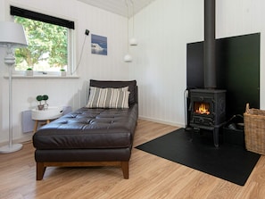 A cozy room with a bed, a small table with a lamp, a window with a view of trees, and a wood-burning stove.