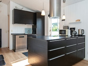 A modern kitchen with a central island, stainless steel appliances, pendant lighting, and a view to the outdoors.