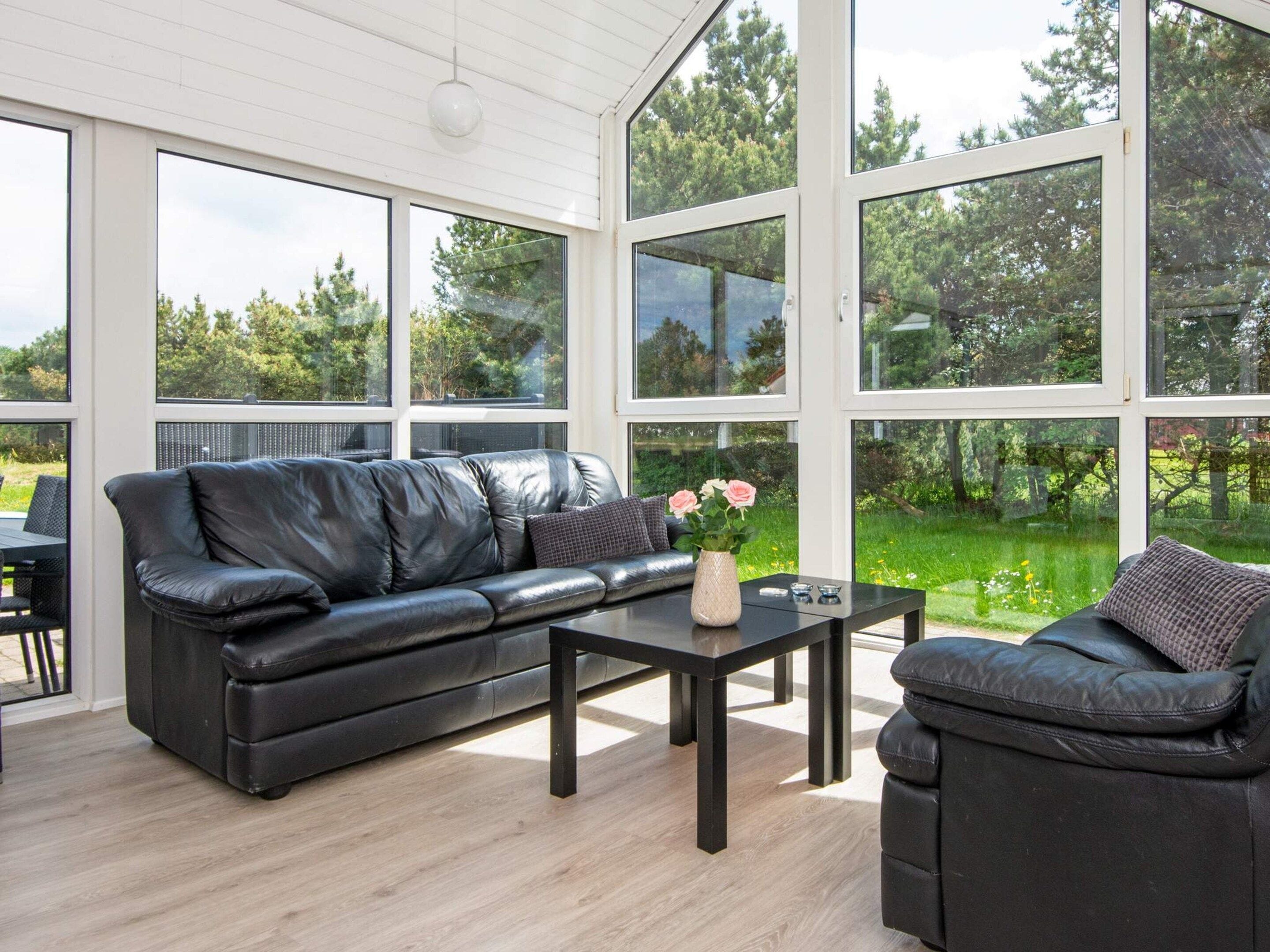 A modern living room with a leather sofa, a coffee table, and a view of a green landscape through large windows.