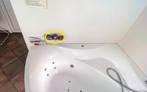 Uma banheira branca com chuveiro manual, um objeto amarelo circulado e uma pequena garrafa na borda.