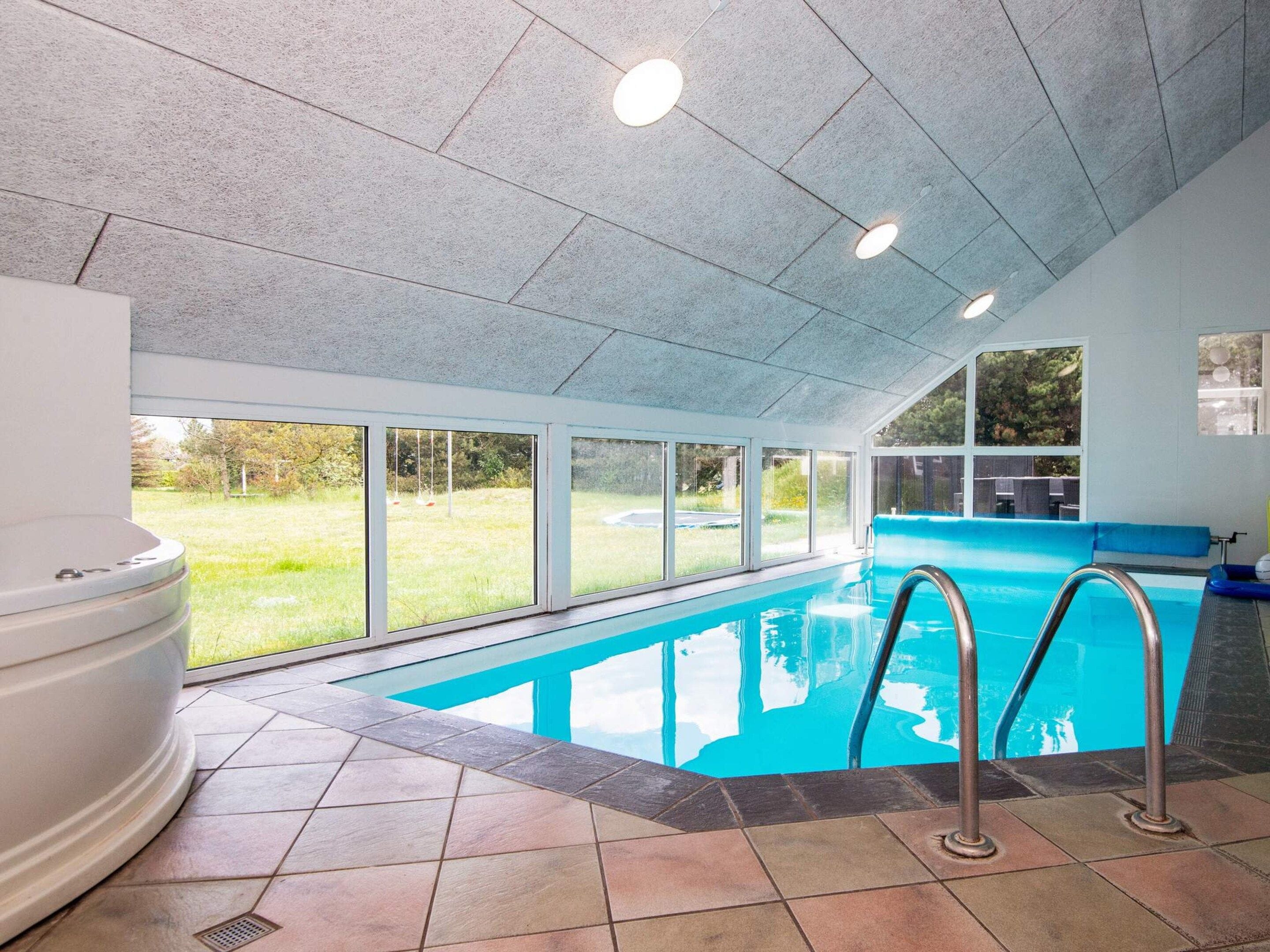 An indoor swimming pool with clear glass walls, a tiled floor, and a hot tub area.