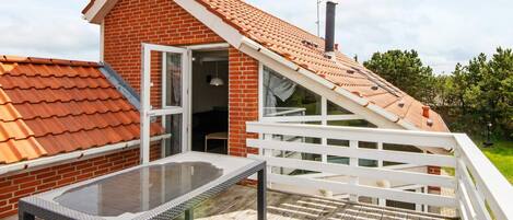 A house with a sloped roof, a glass door entrance, and a wooden deck with a glass table.