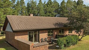 A small brick house with a tiled roof, a covered patio with outdoor seating, and a large tree in the background. - 6 Person Holiday Home in NÃ¸rre Nebel (Norre Nebel)