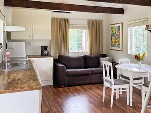A compact living space with a kitchenette, a sofa, a dining table with chairs, and a window with curtains. - 4 Person Holiday Home in Stenhamra (Stenhamra)