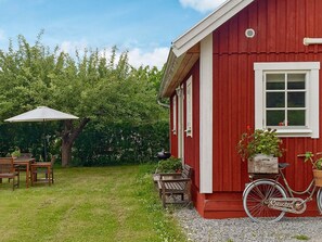 A red building with a white window, a bicycle with a basket, and outdoor furniture. - 4 Person Holiday Home in Stenhamra (Stenhamra)