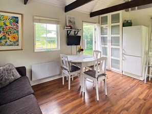 A cozy room with a wooden floor, a white dining table with chairs, a gray sofa, and a white cabinet with glass doors. - 4 Person Holiday Home in Stenhamra (Stenhamra)