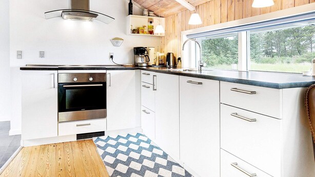 A modern kitchen with white cabinets, a stainless steel oven, a coffee maker, and a window overlooking a garden.