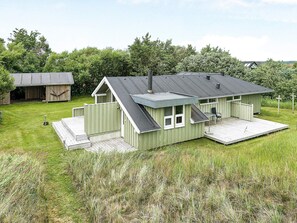 Une maison verte de plain-pied, dotée d’un porche, d’une petite terrasse et d’un garage.