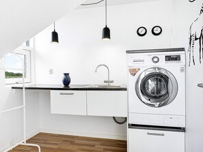 A compact kitchen with a built-in washer and dryer, a window, and a blue vase on the counter.