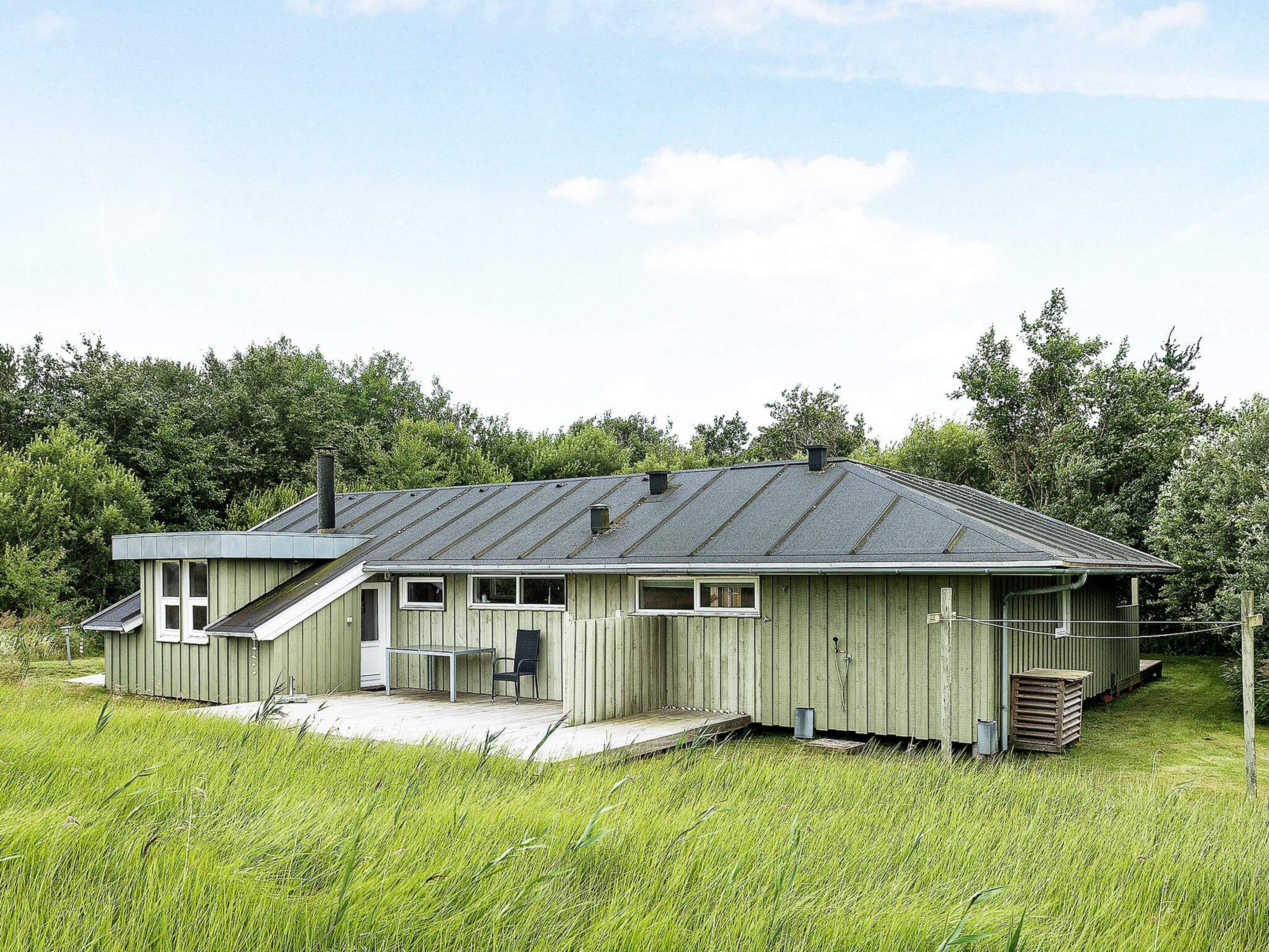 A single-story wooden house with a sloped roof, a porch with a bench, and a small outdoor table.