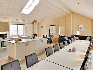 A modern kitchen with a central island, a dining area with a long table and chairs, and a living area with a sofa and a fireplace. - Holiday Home in Kappeln (Kappeln)