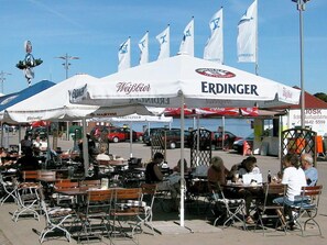 An outdoor dining area with tables and chairs under a large white tent with flags.