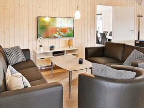 A modern living room with a flat-screen TV, leather sofas, a coffee table, and a wooden wall. - Holiday Home in Kappeln (Kappeln)