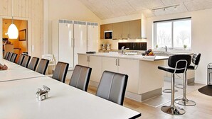 Uma cozinha moderna com uma ilha central, uma área de jantar com uma mesa comprida e cadeiras, e uma grande janela que oferece iluminação natural.