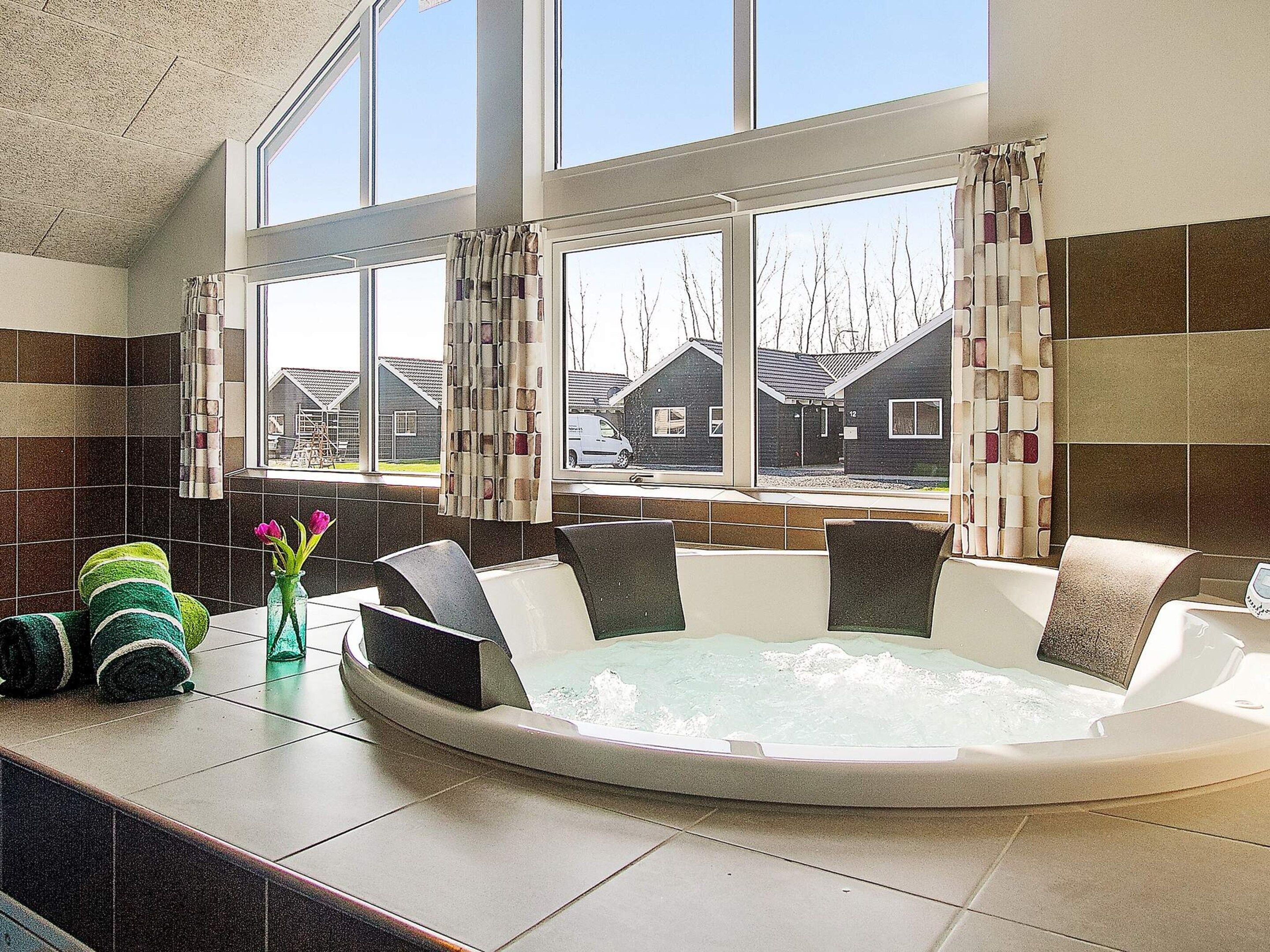 Ein Wellnessbereich mit Whirlpool, Sitzgelegenheiten und Blick auf Häuser durch große Fenster.