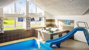 An indoor swimming pool with a slide, a sunlit area with windows, and a tiled wall with a poster. - Holiday Home in Kappeln (Kappeln)