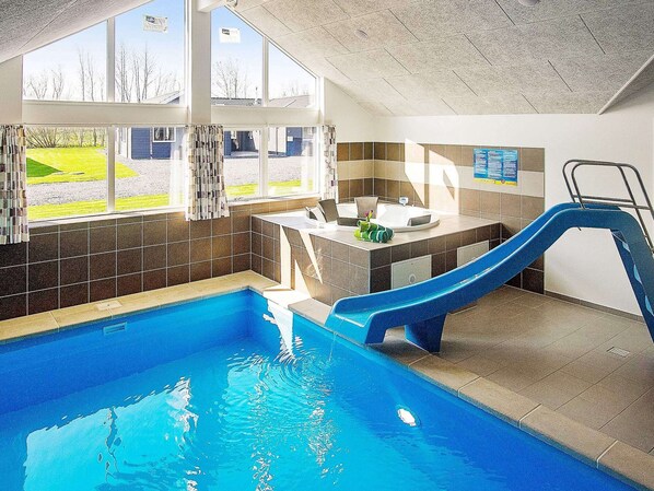 An indoor swimming pool with a slide, a sunlit area with windows, and a tiled wall with a poster. - Holiday Home in Kappeln (Kappeln)