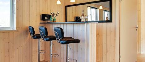 A bar area with three stools, a mirror, and a shelf with bottles.