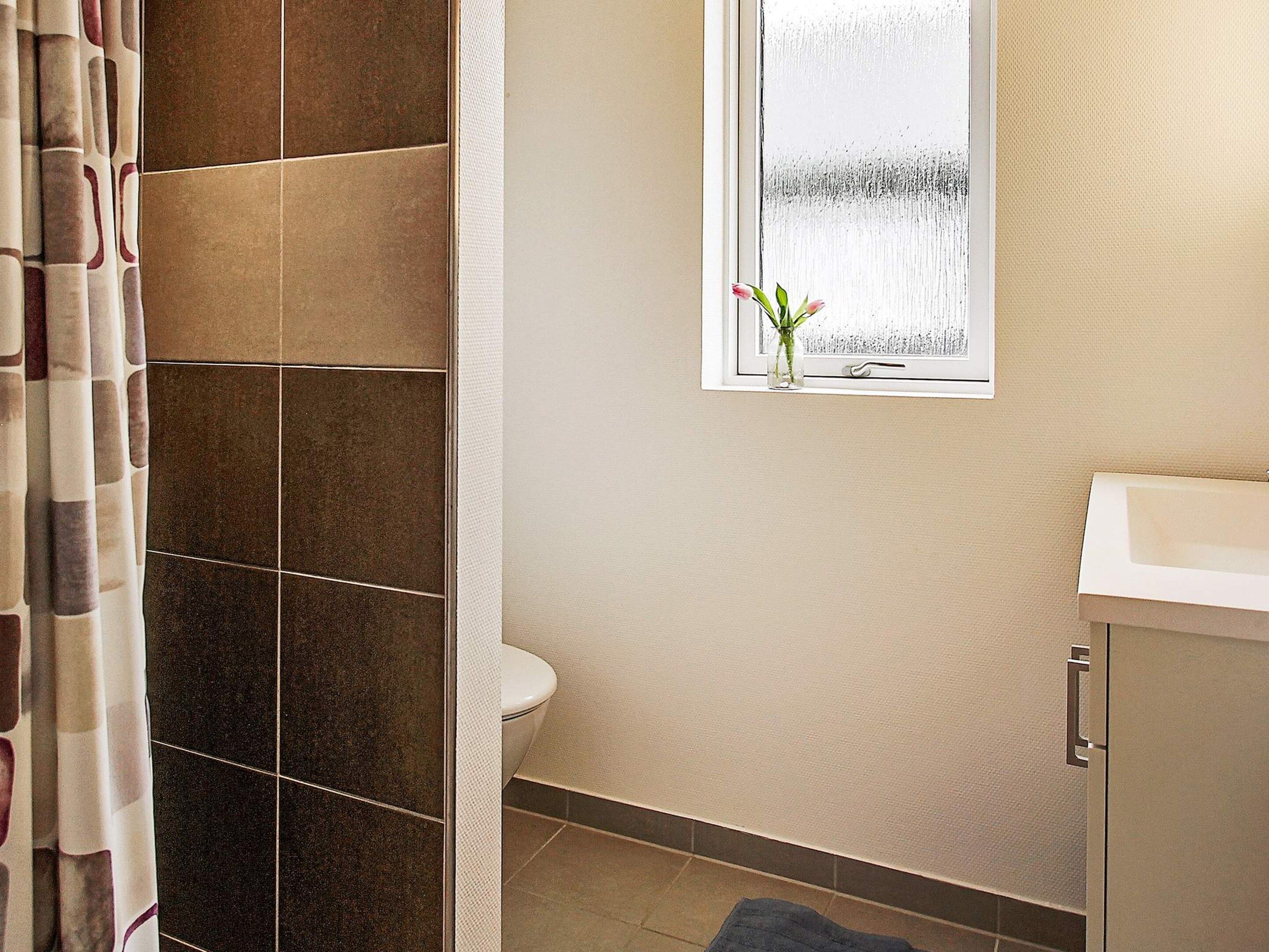A bathroom with a shower, toilet, and a window with a plant.