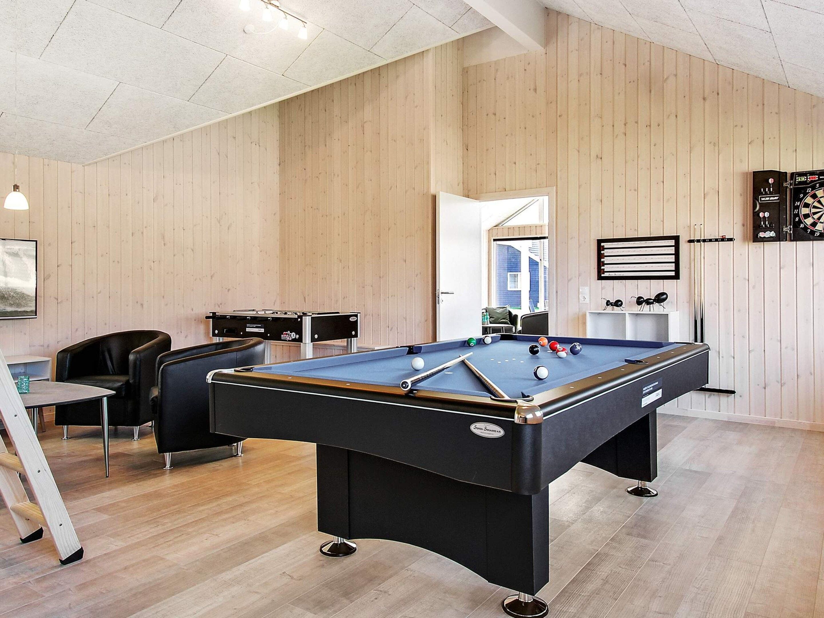 A pool table with balls, a seating area with chairs, and a dartboard on the wall.