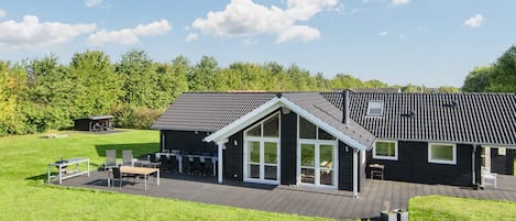 Une maison moderne dotée d’une grande terrasse, d’un espace extérieur aménagé et couvert, et d’une pelouse bien entretenue.