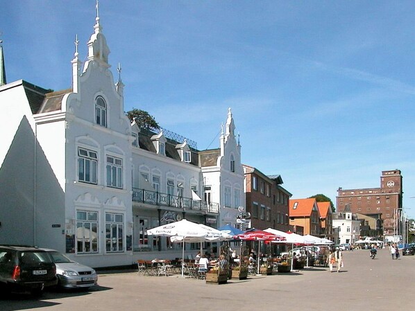 Una plaza con puestos de mercado, un edificio blanco de techo puntiagudo y una torre con campanario.