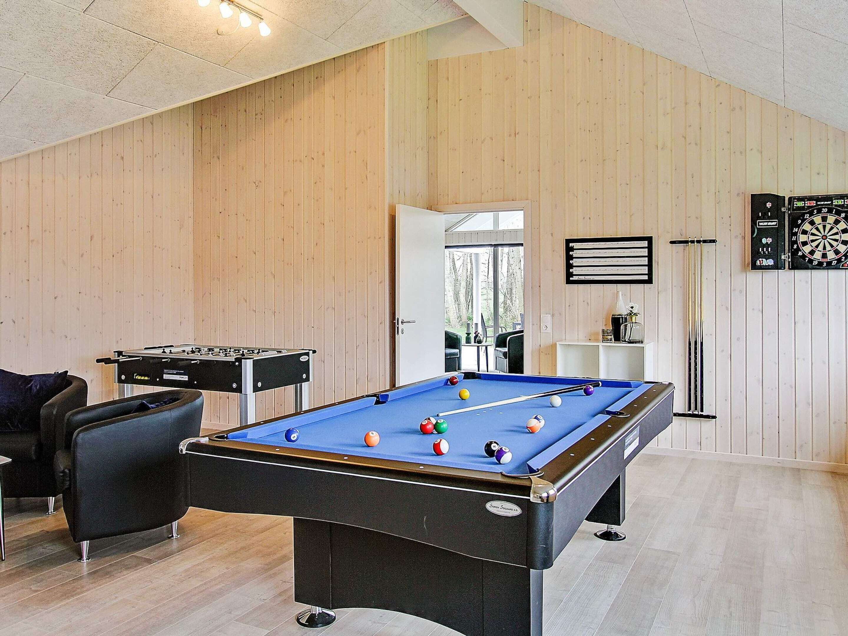 A pool table in a room with wooden walls, a dartboard, and a foosball table.