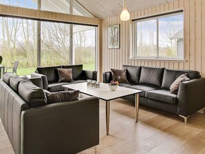 A modern living room with a sofa set, a coffee table, and large windows offering a view of the outdoors. - Holiday Home in Kappeln (Kappeln)