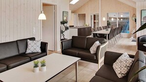 Een modern interieur met houten paneelwanden, een eethoek met een lange tafel en stoelen, en een zithoek met banken en een salontafel.