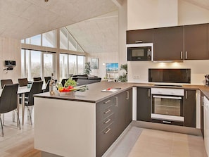 Una cocina moderna con una isla central, electrodomésticos integrados y un comedor con sillas y mesas.