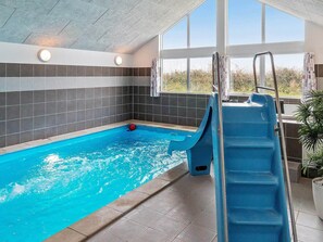 An indoor swimming pool with a slide, tiled walls, and large windows. - Holiday Home in Kappeln (Kappeln)