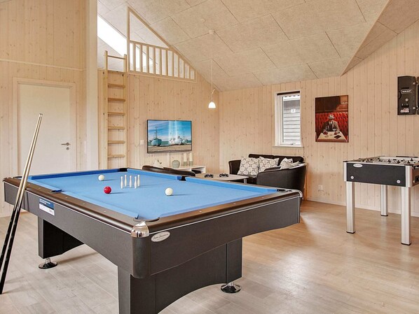A pool table with balls, a foosball table, a sofa, a TV, and a window with blinds.