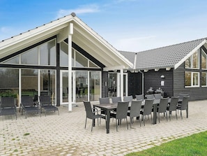 Un patio techado al aire libre con una mesa y sillas, ventanas amplias y una pared exterior oscura.