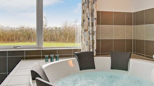 Een jacuzzi met vier stoelen, een raam met uitzicht op een grasveld en een betegelde muur.