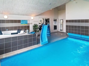 An indoor swimming pool with a blue slide, a hot tub, and a wall-mounted information board. - Holiday Home in Kappeln (Kappeln)
