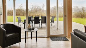 Een kamer met een grote schuifglazen deur die leidt naar een terras buiten, met een tafel en stoelen.