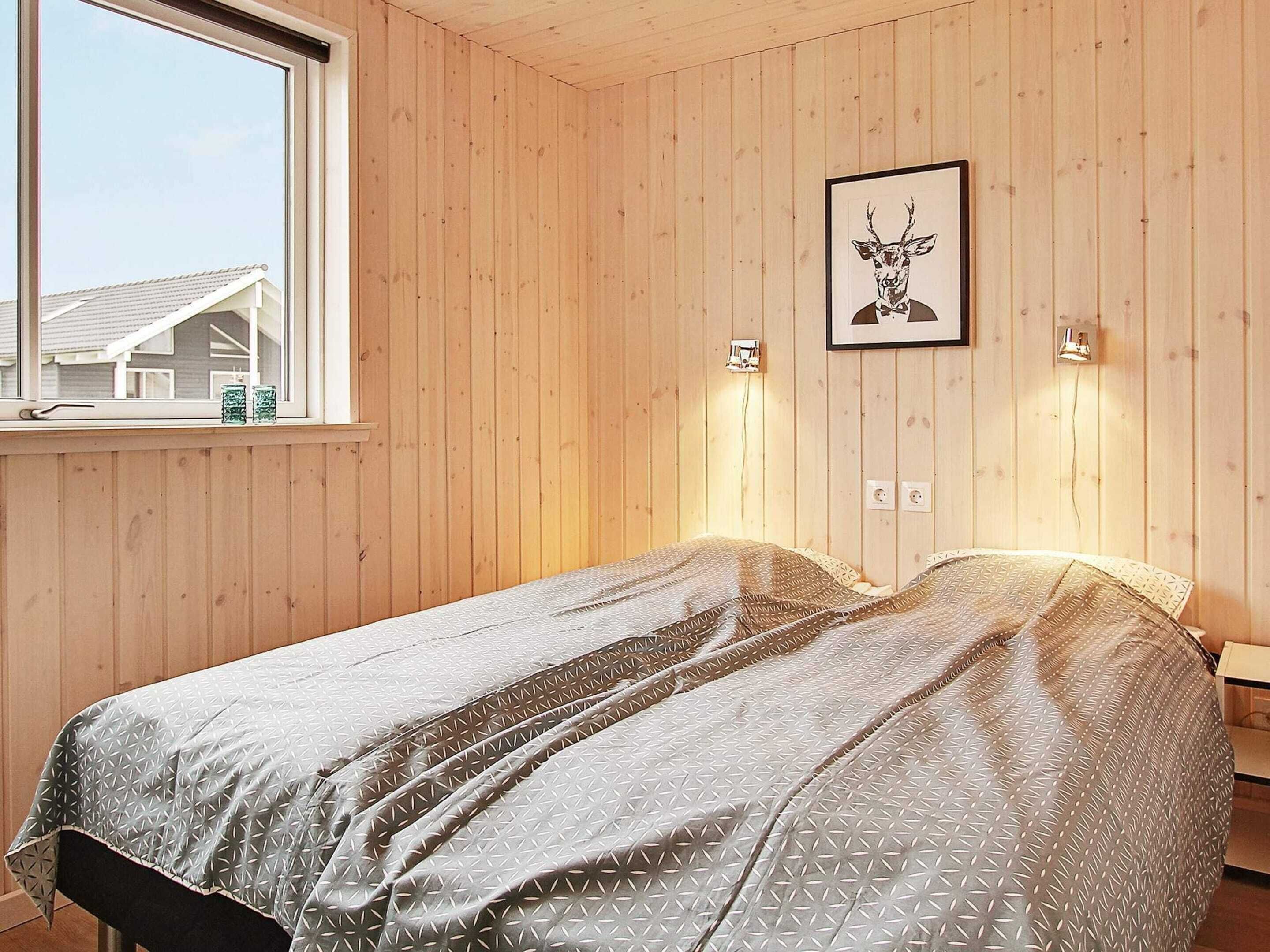 A wooden-paneled room with a bed, a framed picture on the wall, and a window.