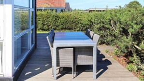 An outdoor patio with a table and chairs, surrounded by greenery and a building with large windows. - 4 Star Holiday Home in Hadsund (Hadsund)