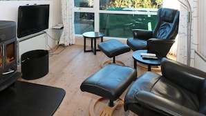 A cozy living room with a fireplace, leather seating, a TV, and a large window with a view of greenery. - 4 Star Holiday Home in Hadsund (Hadsund)