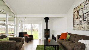 En moderne stue med pejs, to sofaer, et sofabord og et stort vindue med udsigt over naturen.
