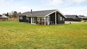 Et moderne hus med en stor græsplæne, en terrasse med et bord og stole, samt en garage.