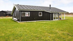 En moderne bygning i sort med skråt tag, store vinduer og et overdækket udendørs siddeområde.