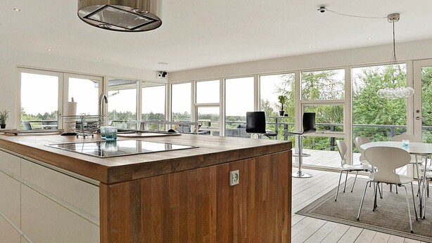 A modern kitchen with a wooden island, large windows, and a deck area with outdoor seating.