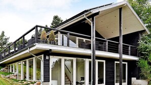 A modern two-story house with a balcony, large windows, and a stone foundation.