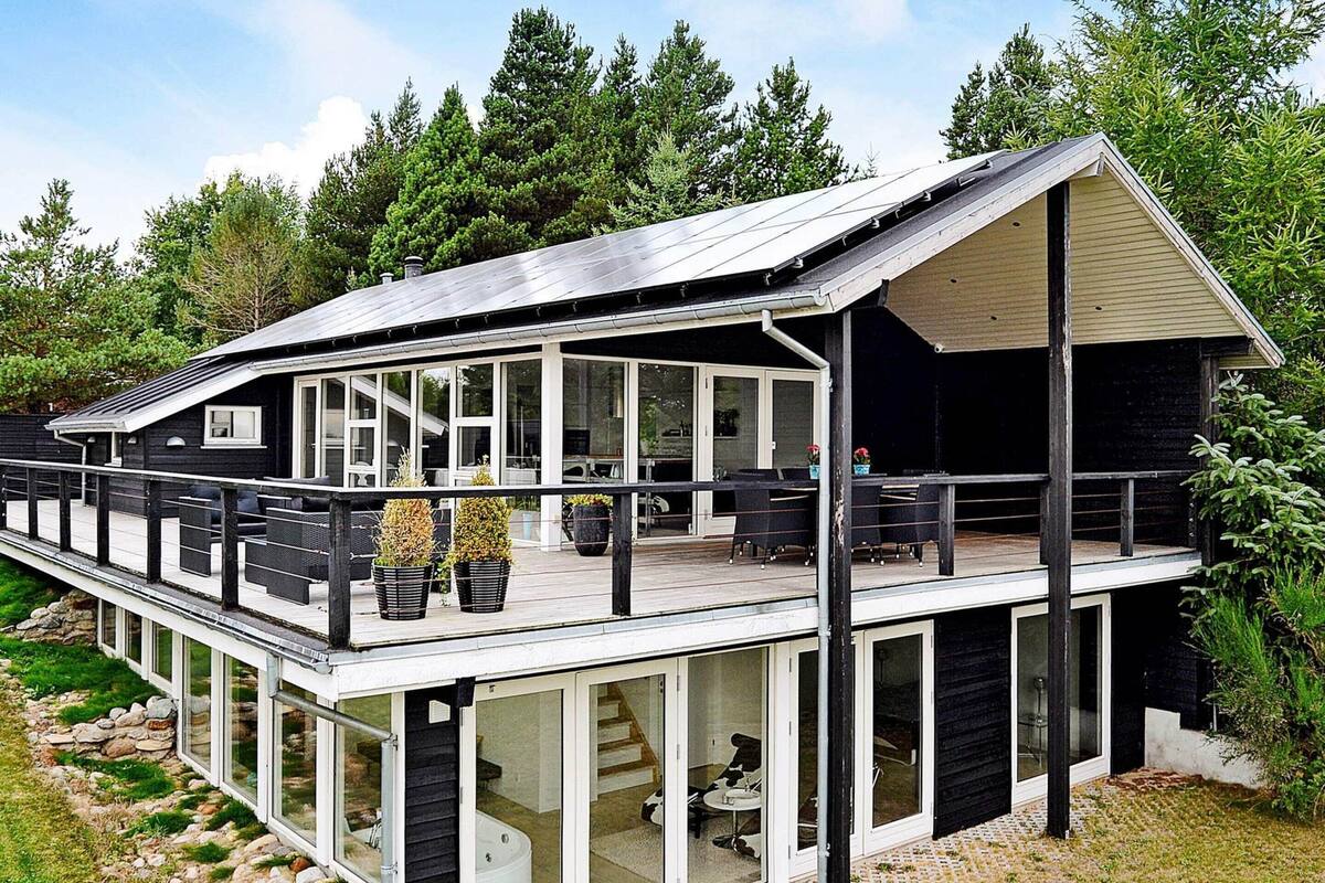A modern house with a covered deck, large windows, and a stone pathway leading to the entrance.
