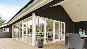 A covered outdoor area with a wooden deck, a seating area with wicker furniture, and a large sliding glass door leading to an interior space.