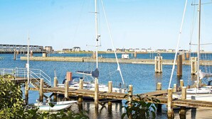 Un port de plaisance avec des bateaux amarrés à des quais en bois, un ciel dégagé et des bâtiments en arrière-plan.