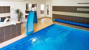 Une piscine intérieure avec un toboggan bleu, un transat et une petite plante.