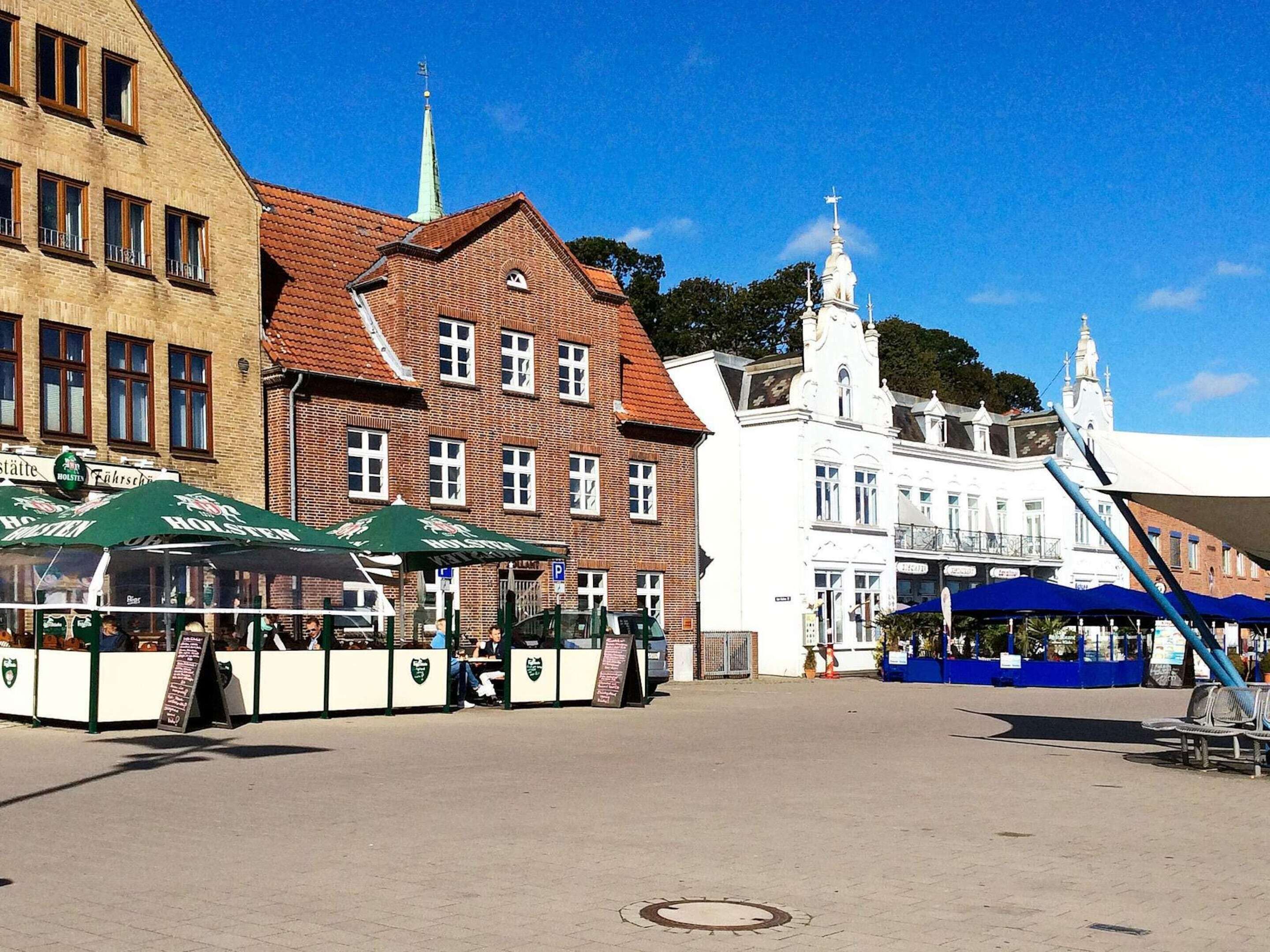 A public square with a beer tent, a white building with a tower, and a brick building with a red roof.